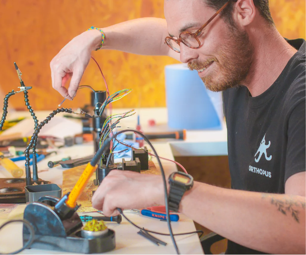 Technician assembling a motorized assistive device with electrical wires and tools on a workbench in a workshop.